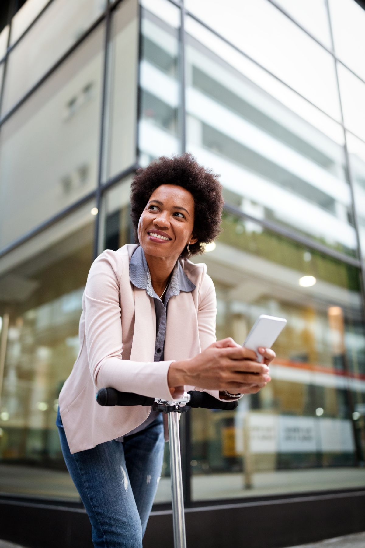 Femme souriante penchée sur un scooter électrique avec un téléphone cellulaire à la main.