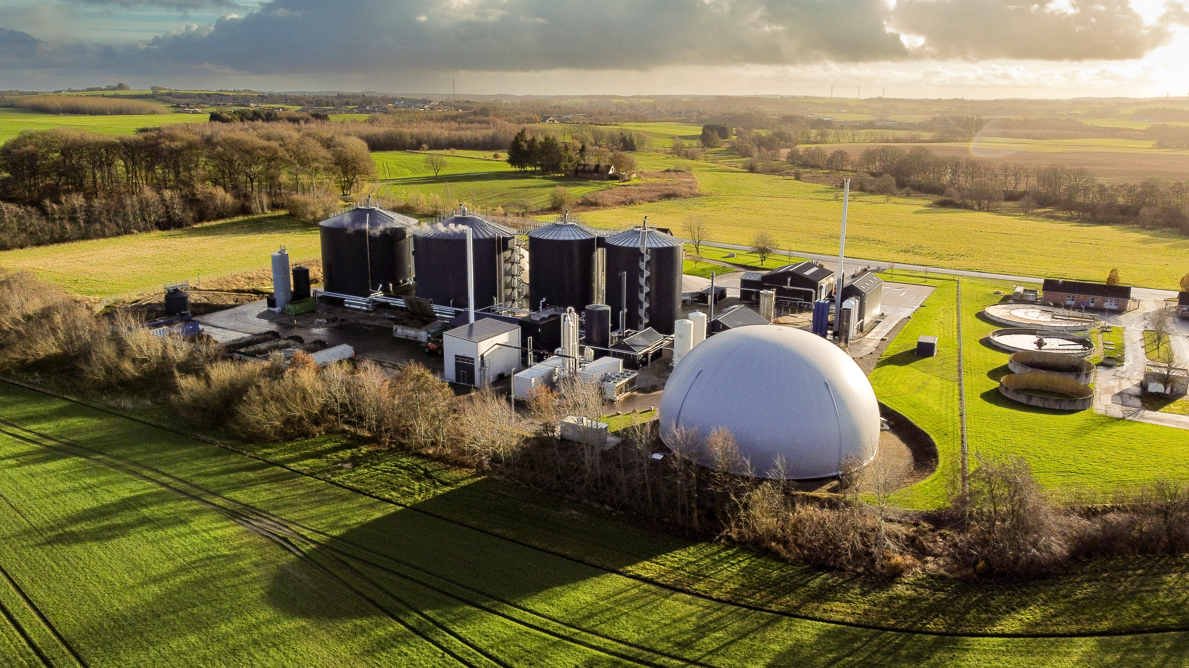 Vue aérienne d'une grande installation de production de biogaz entourée de terres agricoles verdoyantes au Danemark, qui met en valeur l'infrastructure d'énergie renouvelable et la technologie rurale durable.
