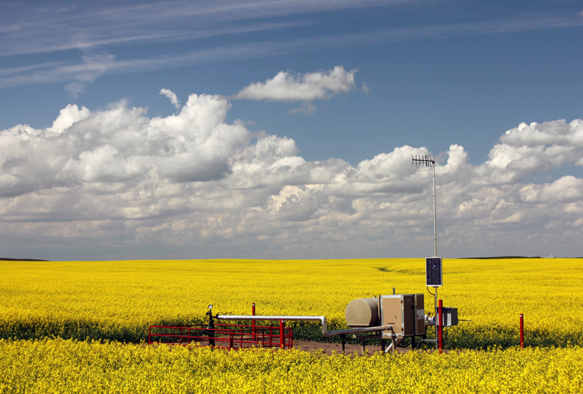 Tête de puits de gaz naturel dans un champ de canola sous un ciel partiellement nuageux