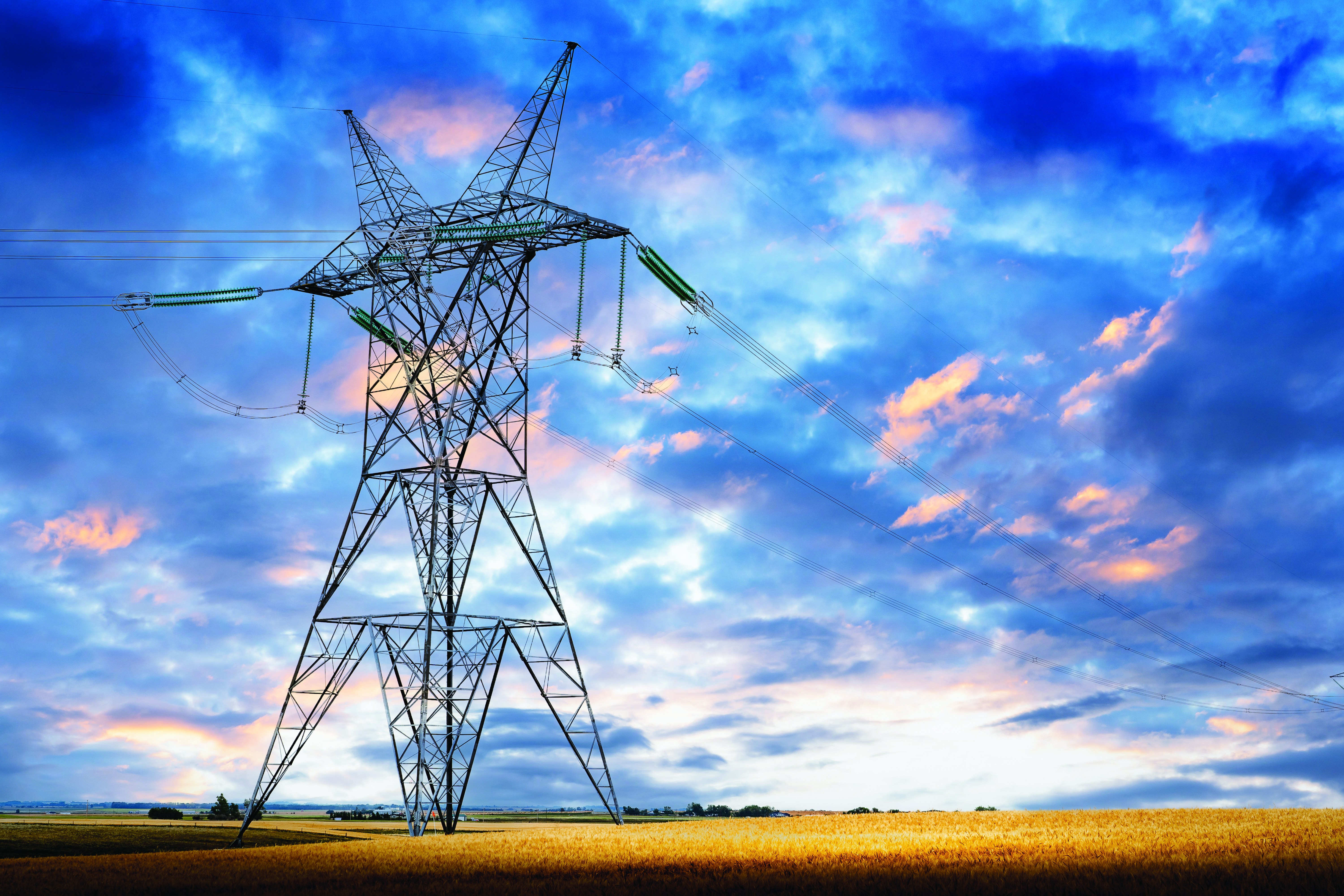 Transmission tower standing tall at sunrise with a cloudy sky on a prairie landscape in Rocky View County Alberta.