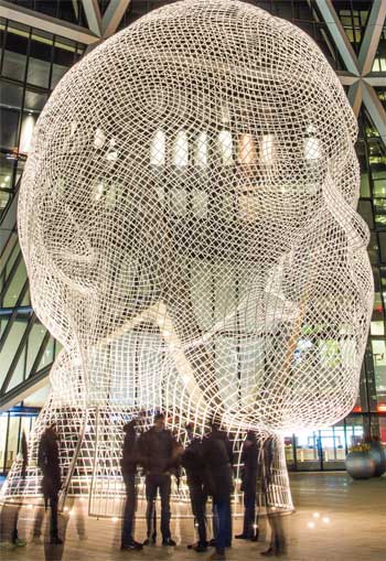 A group of people congregate in front of Jaume Plensa’s “Wonderland” sculpture at night.