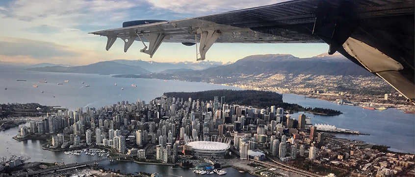 An aerial view of the west end of Vancouver, the Burrard Inlet with transportation tankers, and the mountain ranges in the distance. 