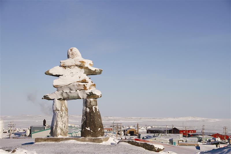 Single Inuksuk or Inukshuk landmark covered in snow on the top of the hill in the community of Rankin Inlet, Nunavut, Canada.