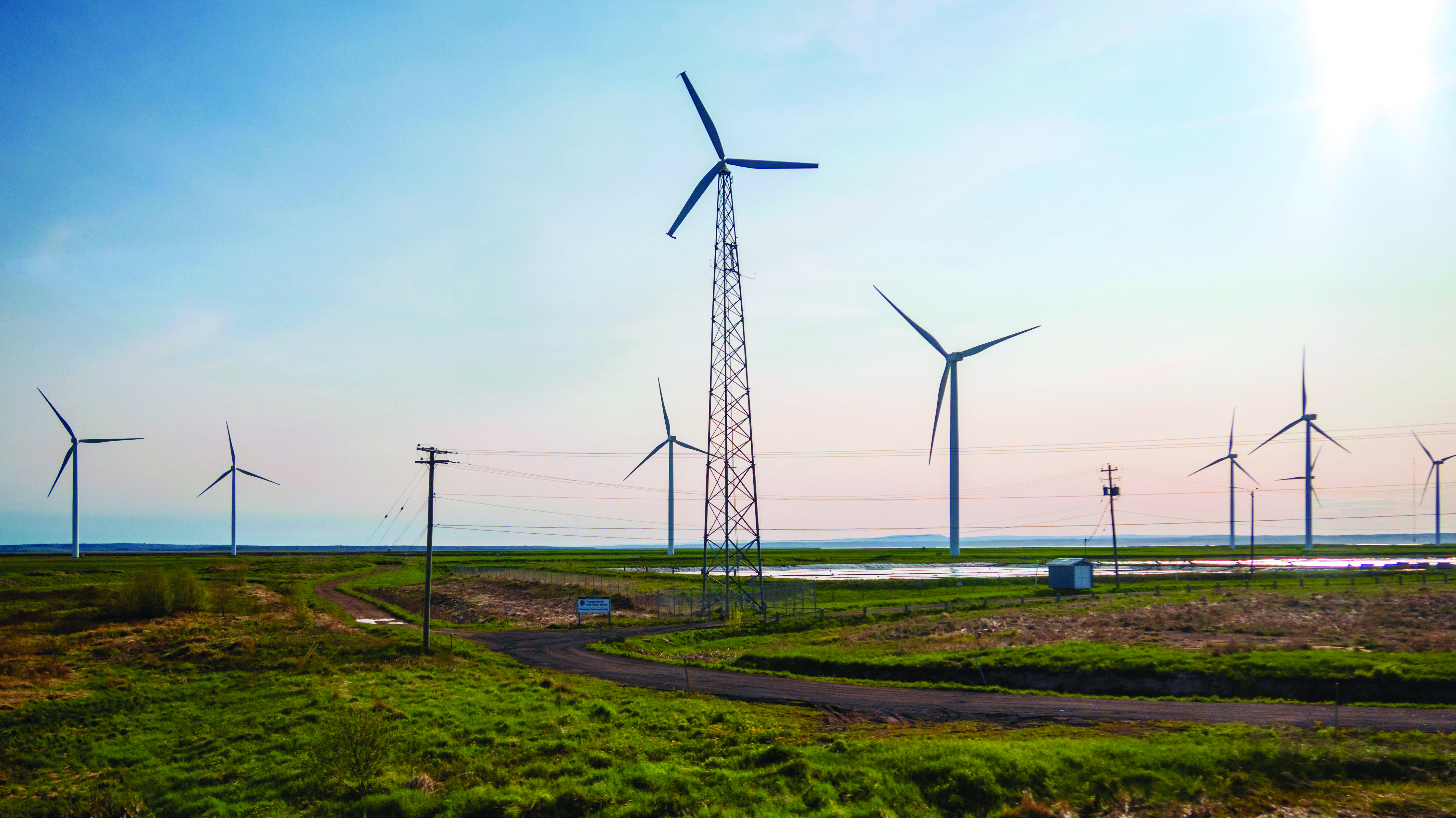 Wind turbines along gravel highway from a wind farm east of Amherst, Nova Scotia in early morning light with partly cloudy skies.