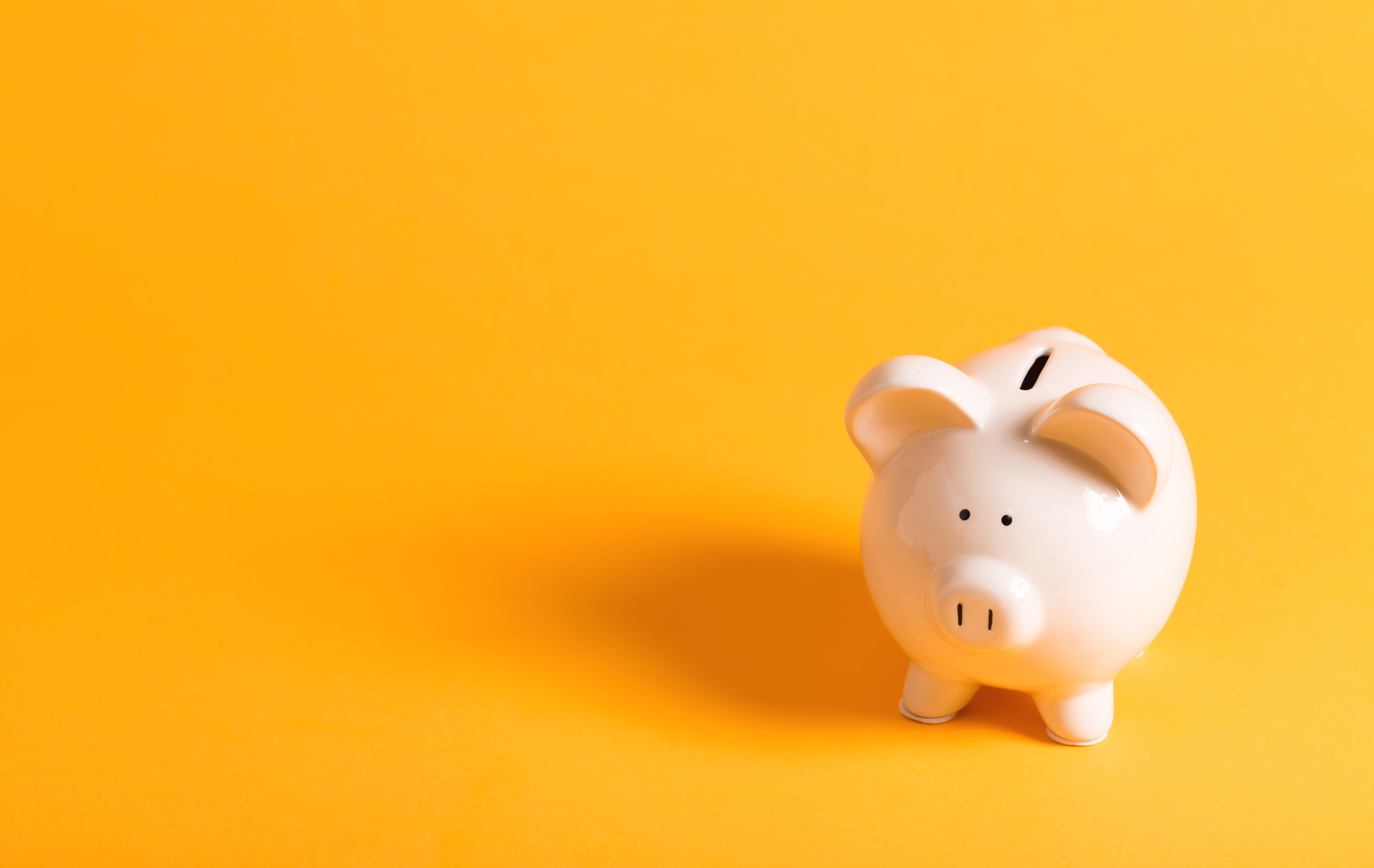 White ceramic piggy bank on yellow background.